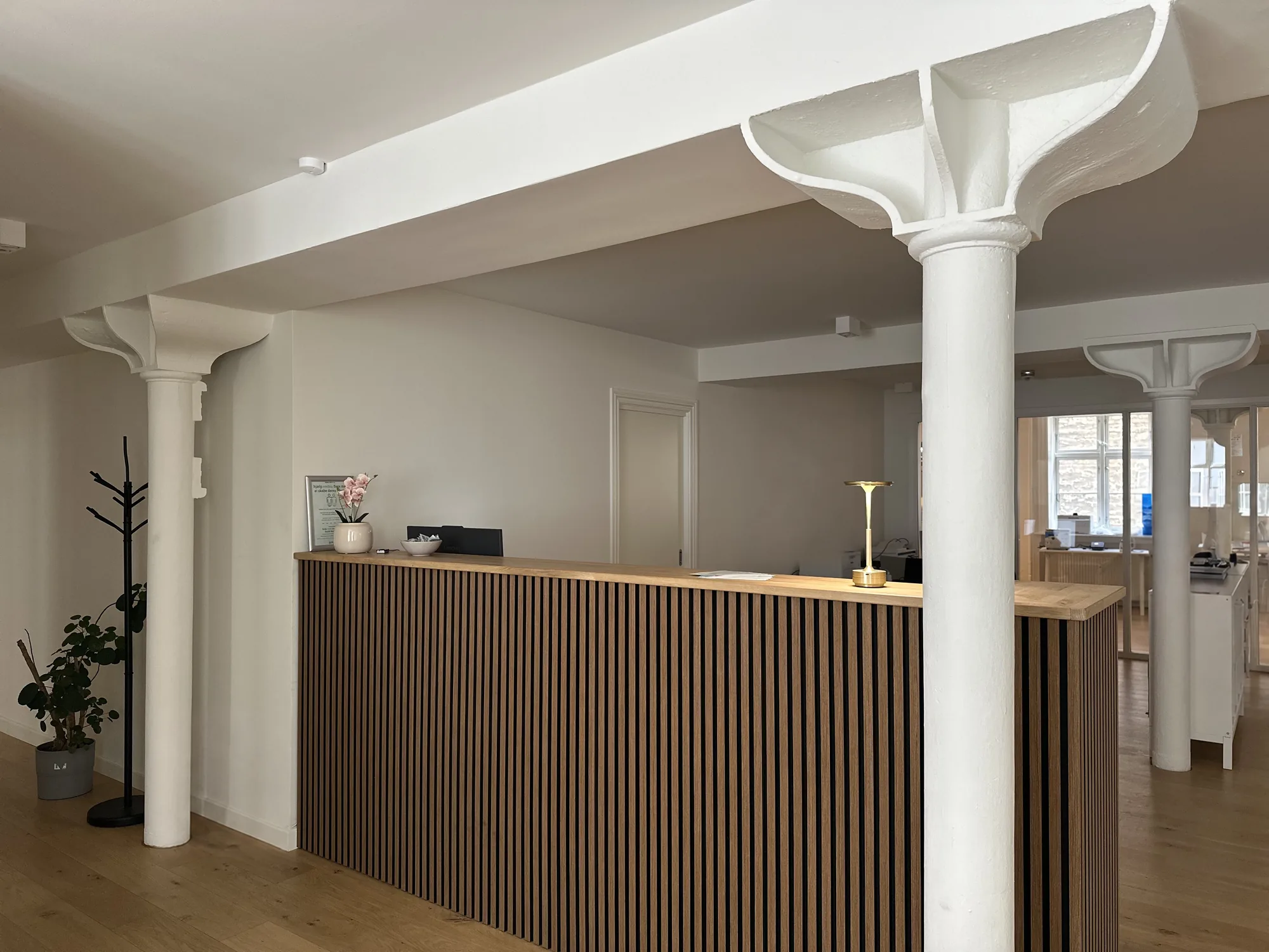 The clinic reception desk with oak slats, white columns, and a brass lamp