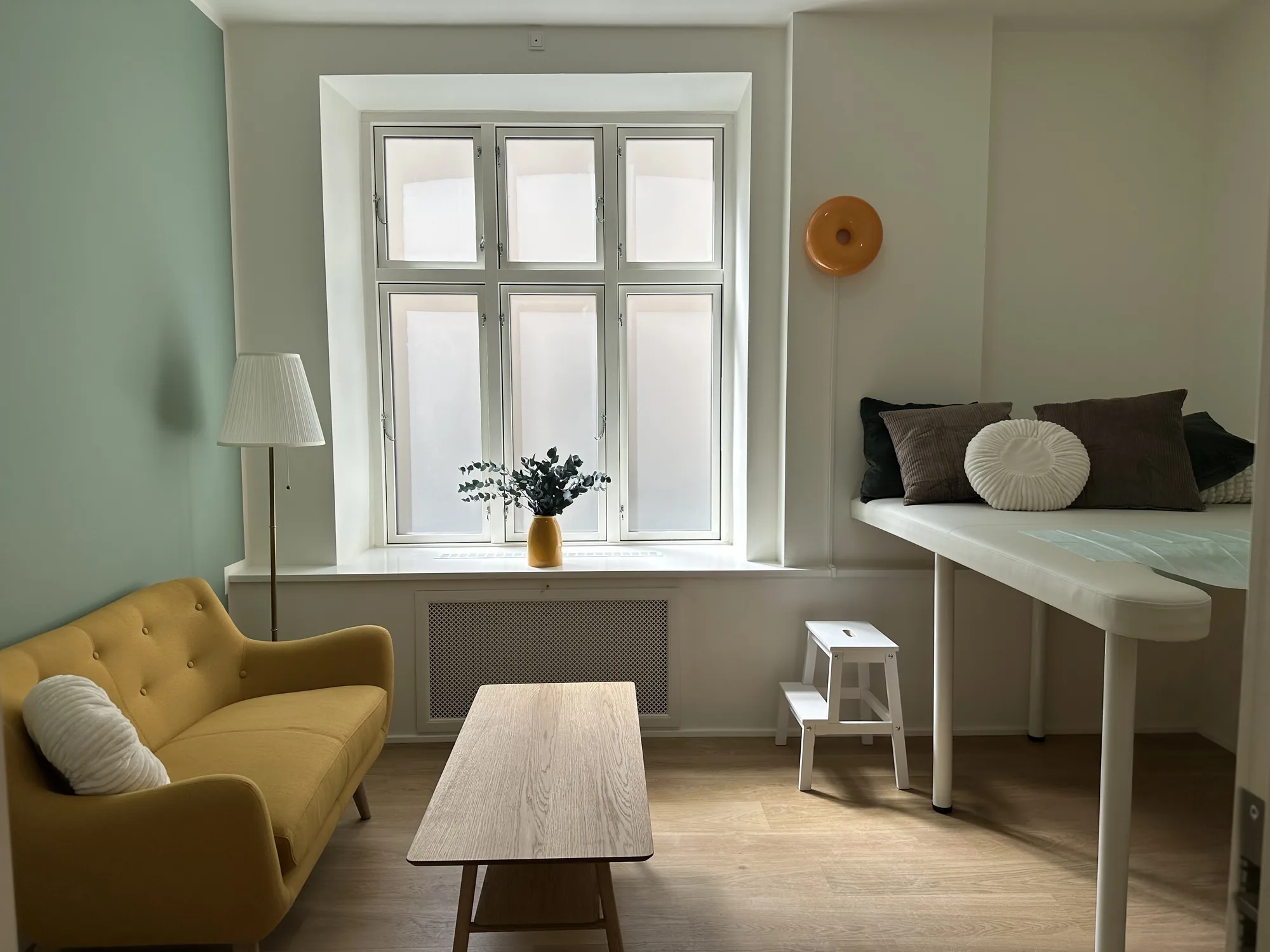 The treatment room with a mustard sofa by the window and the examination bed with soft cushions